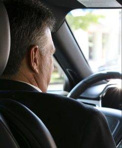 chauffeur driver in black suit driving a Lux Line Transportation sedan